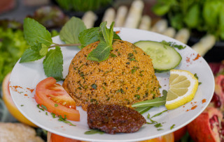 CousCous Salat angerichtet auf einem Teller. Daneben Gemüse wie Tomate & Zitrone