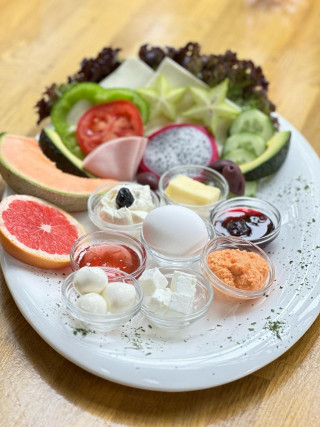 Weißer Teller mit Aufstrichen, Obst, Tomatenscheibe und einem Ei